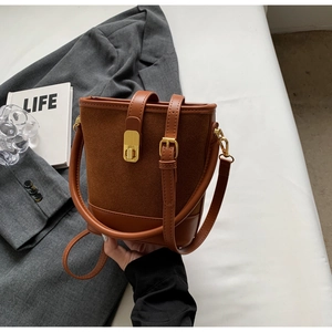 Close-up of brown suede bucket bag with gold clasp and adjustable leather shoulder strap
