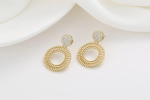 Detailed view of 18K gold mandala earrings with zircon accents on white silk backdrop