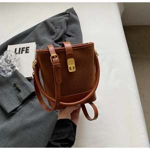 Detail of tan bucket bag with suede leather patchwork and a gold twist-lock closure