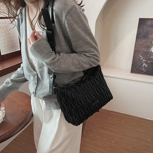 Detail of black matelassé pleated shoulder bag with sleek leather finish on a female model