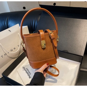 Detail view of caramel brown bucket bag with gold clasp and suede texture in gift box