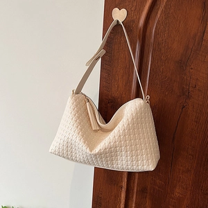 Sac Boston tissé crème avec pompon décoratif suspendu à une porte vintage