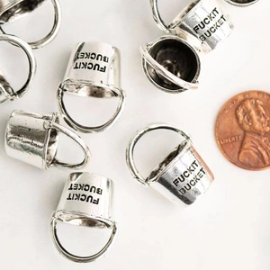 Macro detail of silver bucket pendant with FUCKIT BUCKET engraving beside a coin