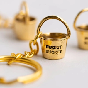 Creative gold metal bucket keychain with Fuckit Bucket engraving in a minimalist style