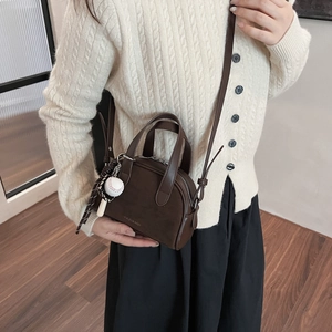 Detail of a dark brown mini handbag with dual handles and a baseball charm