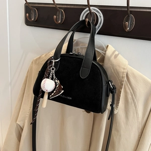 Detail of black mini crossbody bag with sports charm against a beige trench coat