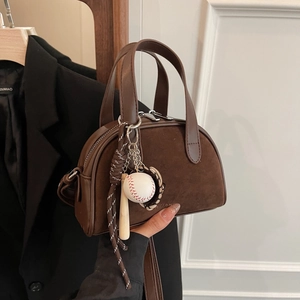 Detail of dark brown mini bowling bag with matte suede texture and baseball charms