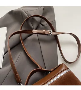 Close-up of adjustable leather shoulder strap with silver buckle on brown crossbody bag