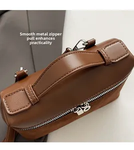 Close-up of dual metal zippers and smooth brown leather top handle for women's crossbody bag