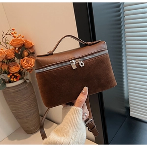 Detail of a brown leather and suede box bag featuring a top handle and metal zipper