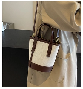 Detail of canvas bucket bag with leather trim and shoulder strap on trench coat outfit
