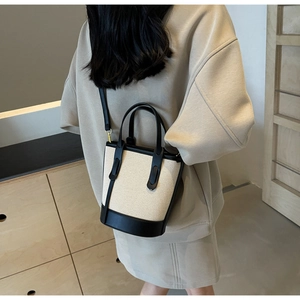 Model view of beige canvas bucket bag with black leather trim and adjustable strap