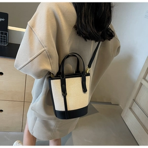 Detail of contrast stitching on beige canvas and black leather bucket bag with gold hardware