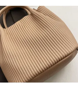 Detail of pleated beige bucket bag showing lychee pattern leather and cylindrical handle