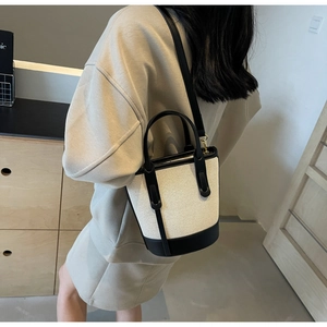 Detail of color-block canvas bucket bag featuring premium black leather trim and gold hardware