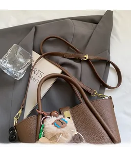 Detail of coffee brown lychee leather handbag with golden metal lock and plush charm