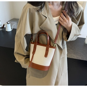 Detailed view of canvas bucket bag with brown leather trim worn with khaki coat