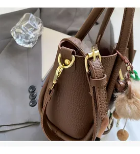 Close-up of dark brown lychee grain leather bucket bag with golden hardware and pompom