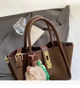 Close-up of brown lychee grain leather bucket bag with gold hardware and plush charm