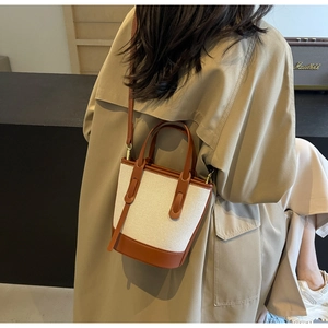 Detail of color-block canvas and leather bucket bag on a model wearing a trench coat
