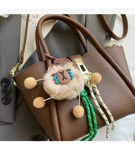 Detail of brown litchi pattern leather bag with lion plush pendant and braided ropes