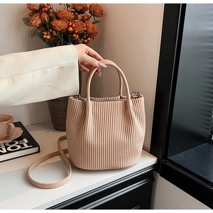 Detailed macro view of the pleated texture and round handle on a beige bucket bag