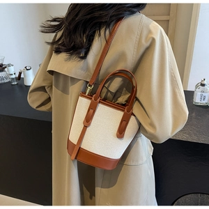 Detail of a contrast color bucket bag in beige canvas and brown leather on a model