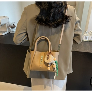 Detail of camel lychee texture bucket bag with gold clasp, pendant, and ribbon strap