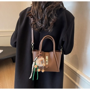 Detailed view of brown lychee leather bucket bag with gold lock and lion charm accessory