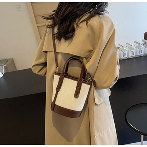 Detail of canvas bucket bag with brown leather trim shown on shoulder in lifestyle setting