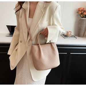 Detail of apricot pleated handbag with crossbody strap shown in a professional office setting