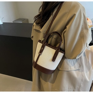 Detail of canvas bucket bag with brown leather trim shown on khaki trench coat