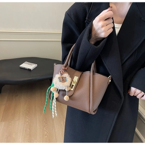 Detail of brown litchi pattern leather handbag with cute lion plush charm and metal clasp
