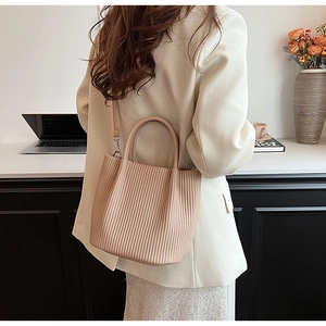 Chic beige pleated bucket bag with round handle shown in a modern lifestyle setting