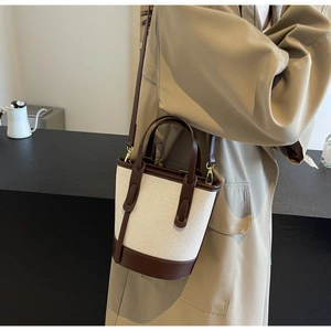 Detail of a beige canvas bucket bag with brown leather trim and gold hardware