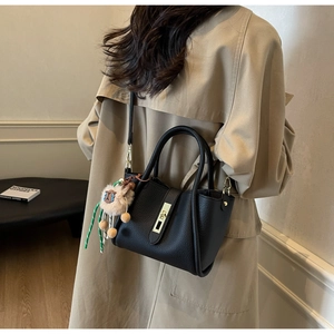Detail of black lychee grain leather handbag with gold buckle and cute alpaca pendant