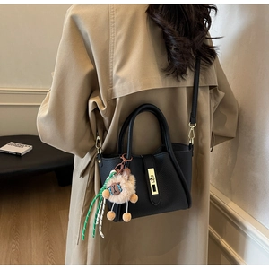 Detail of black lychee leather bag with gold buckle lock and plush charm accessory