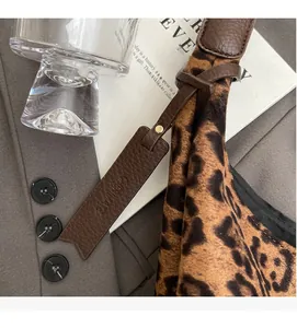 Detail of leopard print tote bag featuring brown leather strap and brand logo tag