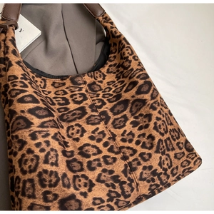 Detailed view of the leopard print texture and sturdy brown leather handles on tote bag