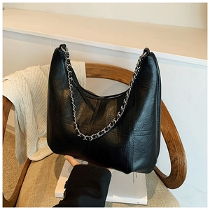 Detail of black textured leather hobo bag with silver chain strap on a wooden chair