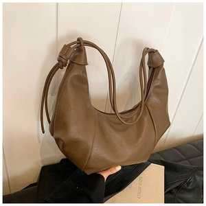 Detail of dark brown ruched hobo bag featuring a decorative knot on the shoulder strap