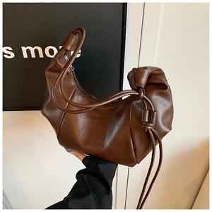 Detail of dark brown croissant bag featuring pleats, knotted strap, and glossy leather texture