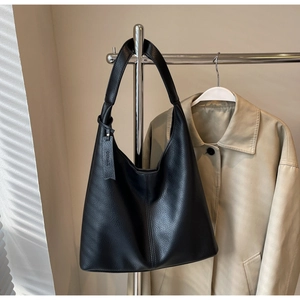 Detail of black lychee grain leather hobo bag with wide strap on a beige coat background