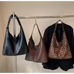 Three hobo tote bags in black leather, brown leather, and leopard print on a display rack