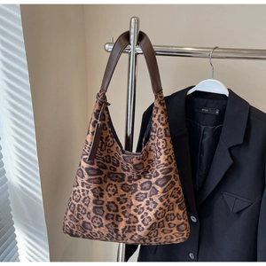 Detail of leopard print tote bag with brown leather strap hanging on a metal rack