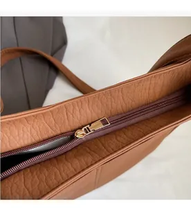 Detail of smooth light gold metal zipper and lychee pattern leather on brown tote bag