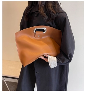 Detail of caramel leather handbag featuring oval silver metal handle and magnetic closure