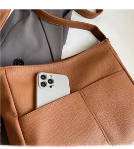 Detail of a brown leather tote bag showing a functional front pocket and texture