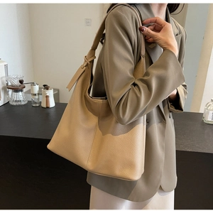 Detail of large beige leather tote bag featuring a textured pebbled finish and wide shoulder strap