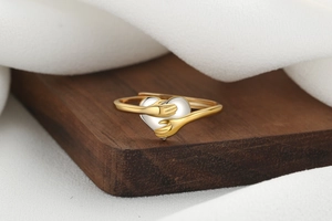 Macro shot of two-tone embrace heart ring featuring gold arms on a wooden display